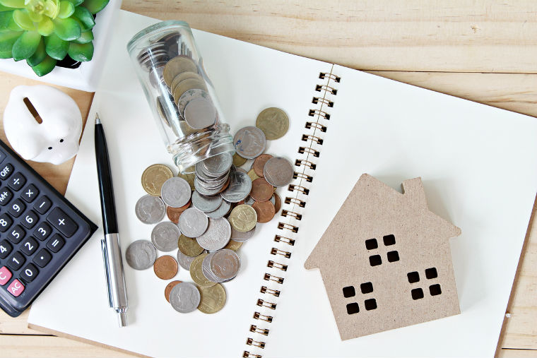 Hauskaufwunsch und Finanzierungsmöglichkeiten kreativ dargestellt mit Pappehaus, Münzgeld und Taschenrechner