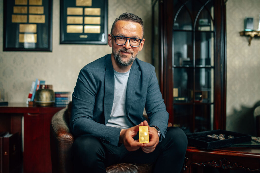 Ronny Wagner im Anzug hält einen Goldbarren in einem stilvollen Büro