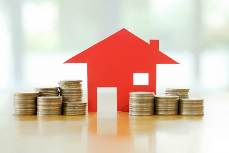 Umfinanzierung Eigenheim- rotes Haus aus Papier mit zwei Münzstapeln davor