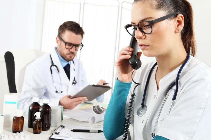Arzthelferin am Telefon im Vordergrund, Arzt im Hintergrund